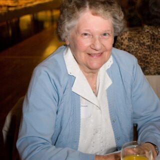Woman holding a glass of orange drink at a social gathering.