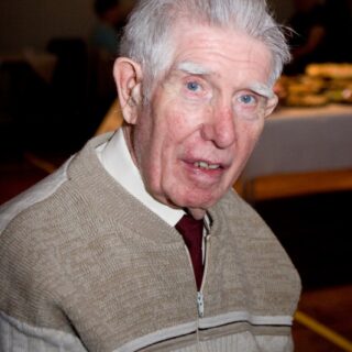 Man seated indoors, looking toward the camera.