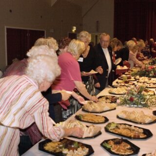 Large group of adults gathered around a buffet table at a community event.