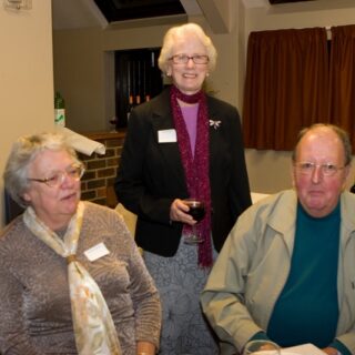 Three individuals gathered near a refreshment table at a social event.