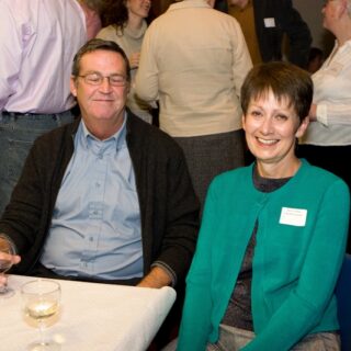 Two attendees seated at a table, one smiling and one holding a glass of red wine.