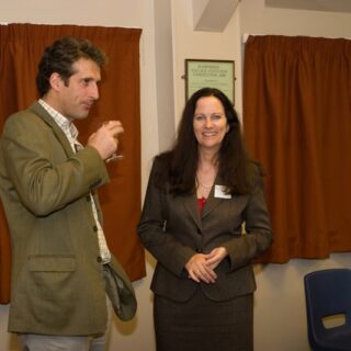 Two people standing indoors, chatting at a formal gathering.