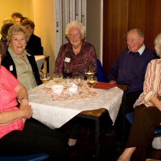 Five guests with name badges seated at a table with wine glasses at the Basinga’s 35th anniversary celebration.