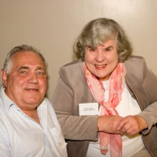 Two attendees seated together, one wearing a name badge for the Building Committee, at the Basinga’s 35th anniversary.