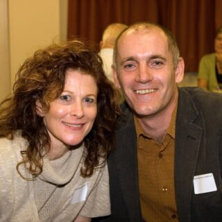 A man and woman sit together at the anniversary event, both wearing name badges.